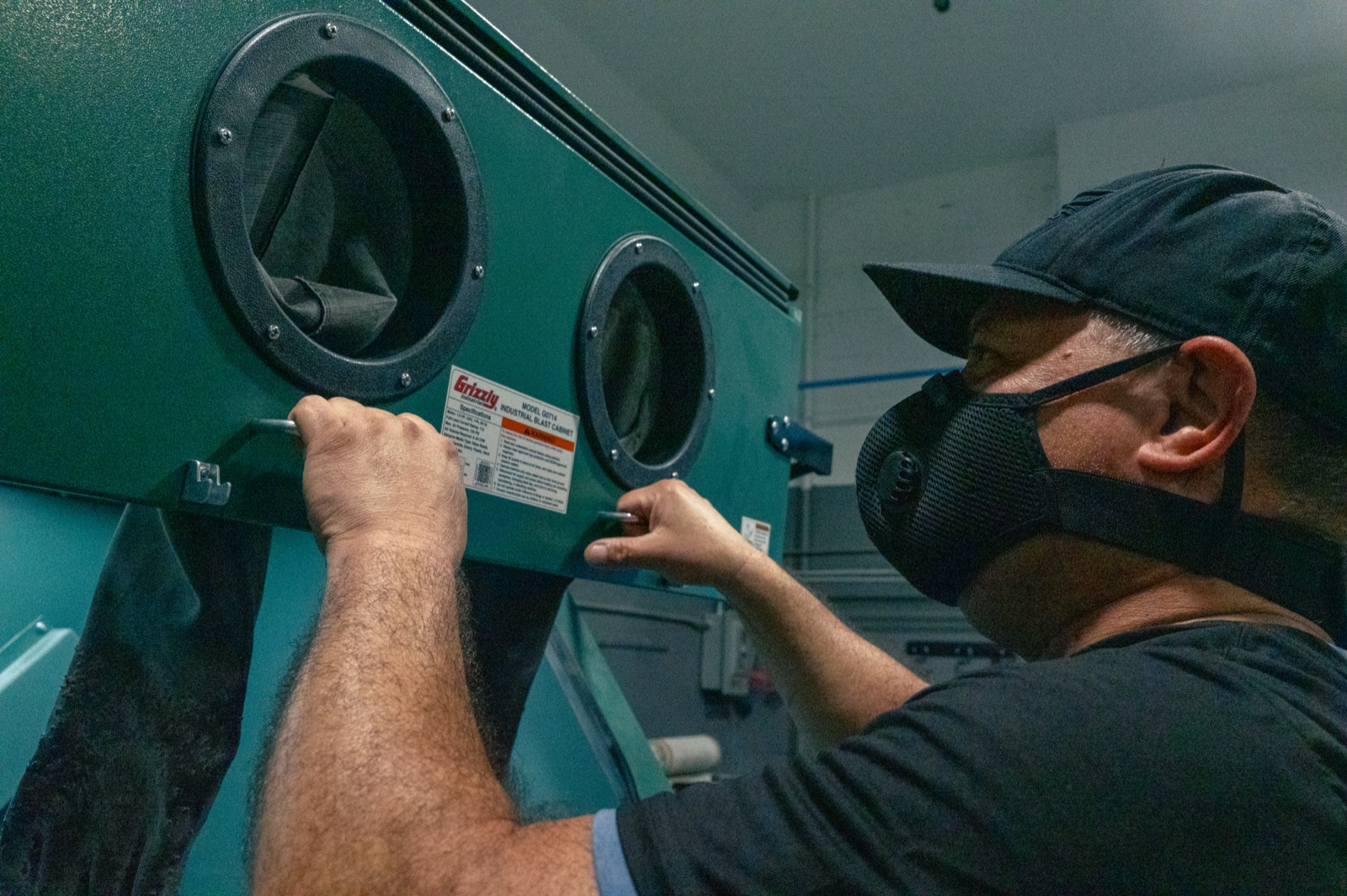 Technician placing a machined part into a bead blasting cabinet