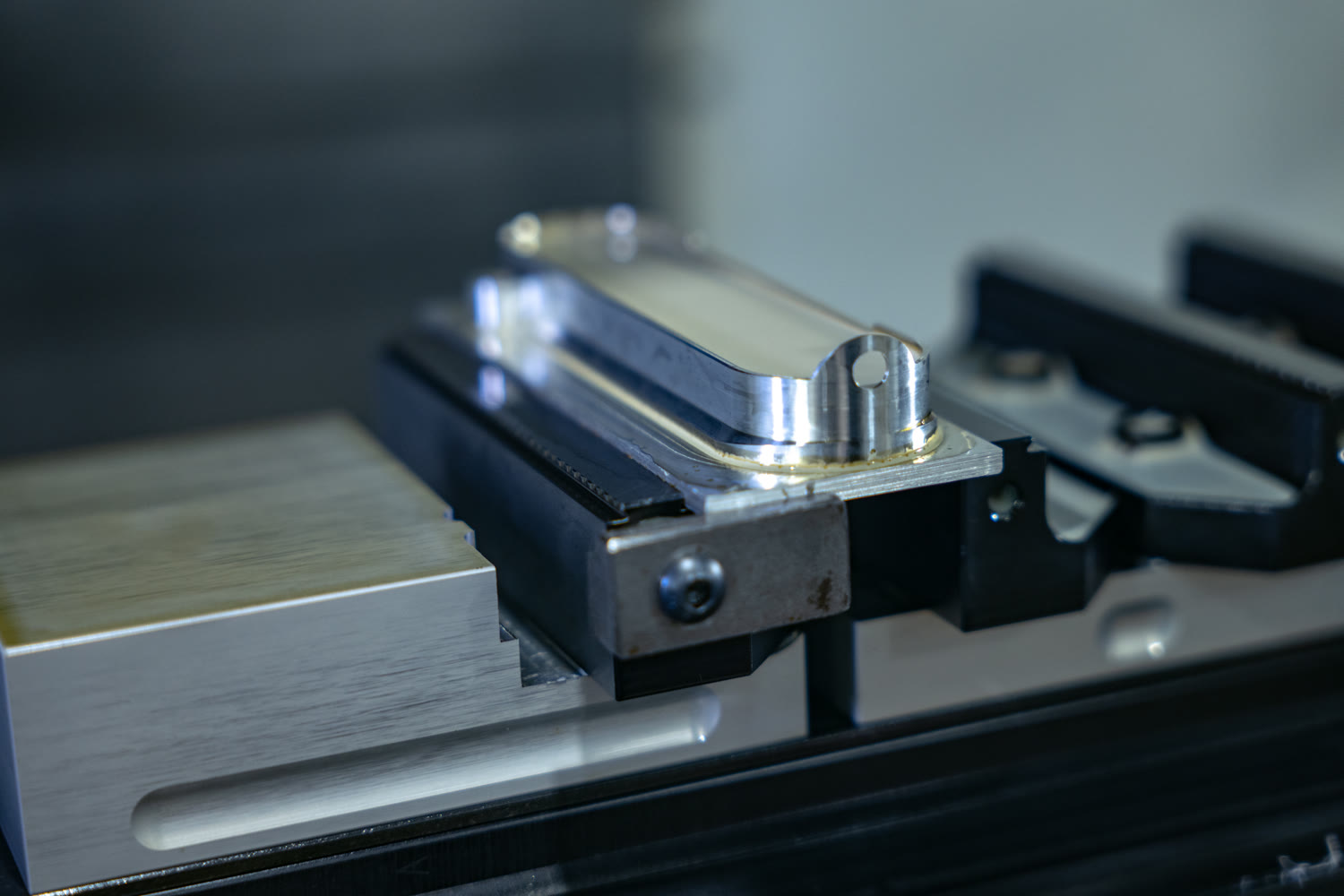 Machined aluminum cover part clamped in a precision vise inside a CNC mill