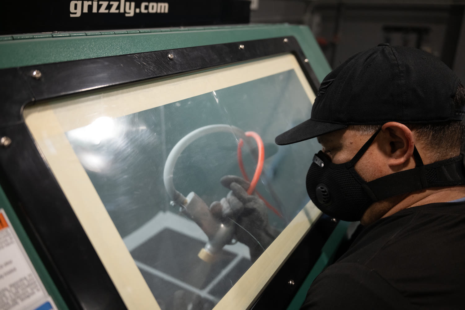 Machinist bead blasting a machined part inside a finishing cabinet