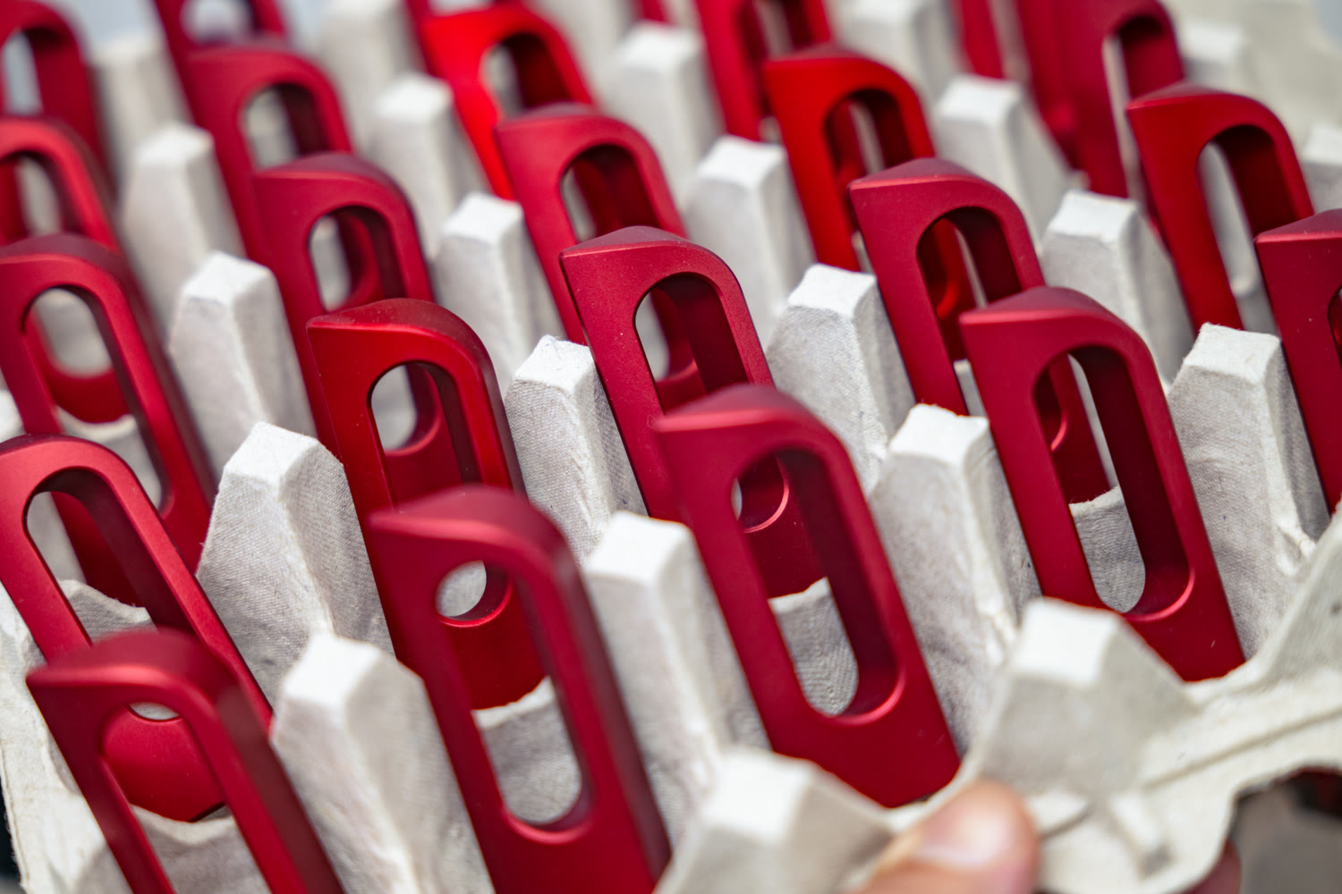 Red anodized CNC machined aluminum parts lined up in molded pulp packaging trays